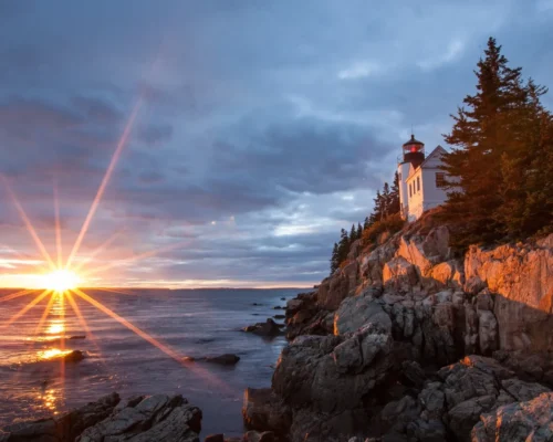 White lighthouse and manor near a cliff leading into the ocean during sunset