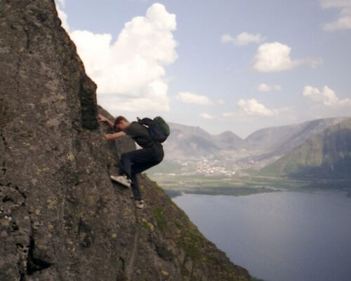 Man wearing a backpack climbing up a cliffside